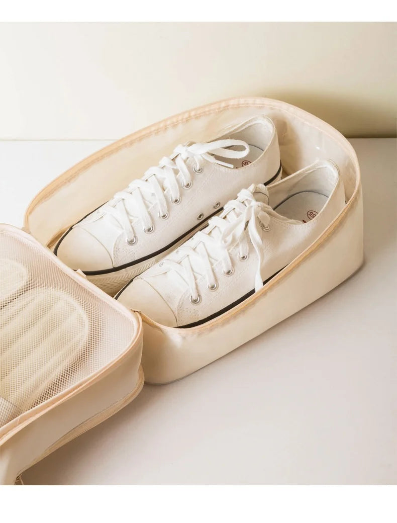 A pair of white canvas shoes is placed inside a beige portable luggage shoe organizer bag.