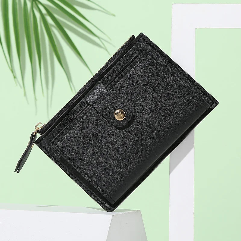 A black PU leather mini card holder wallet is shown diagonally against a light green background.