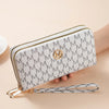 A light beige patterned double zipper wallet with a gold accent is shown being held by a hand.