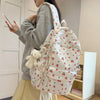 Una persona sostiene una mochila blanca con estampado floral y múltiples bolsillos, junto a una blusa color crema y una falda