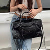 A woman holds a black saddle-shaped PU leather city tote bag against a white car.