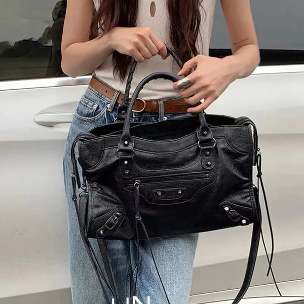 A woman holds a black saddle-shaped PU leather city tote bag against a white car.