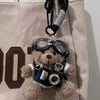 A charming plush bear keychain featuring glasses and a camera attached to a black strap.