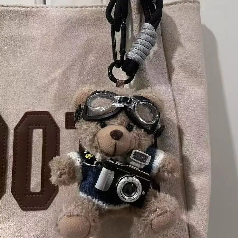 A charming plush bear keychain featuring glasses and a camera attached to a black strap.