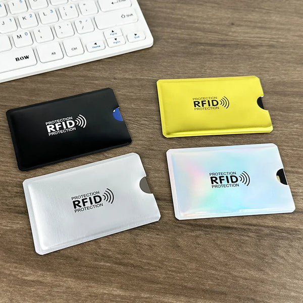 Three RFID blocking card sleeves in black, yellow, and clear plastic are displayed on a wooden surface.