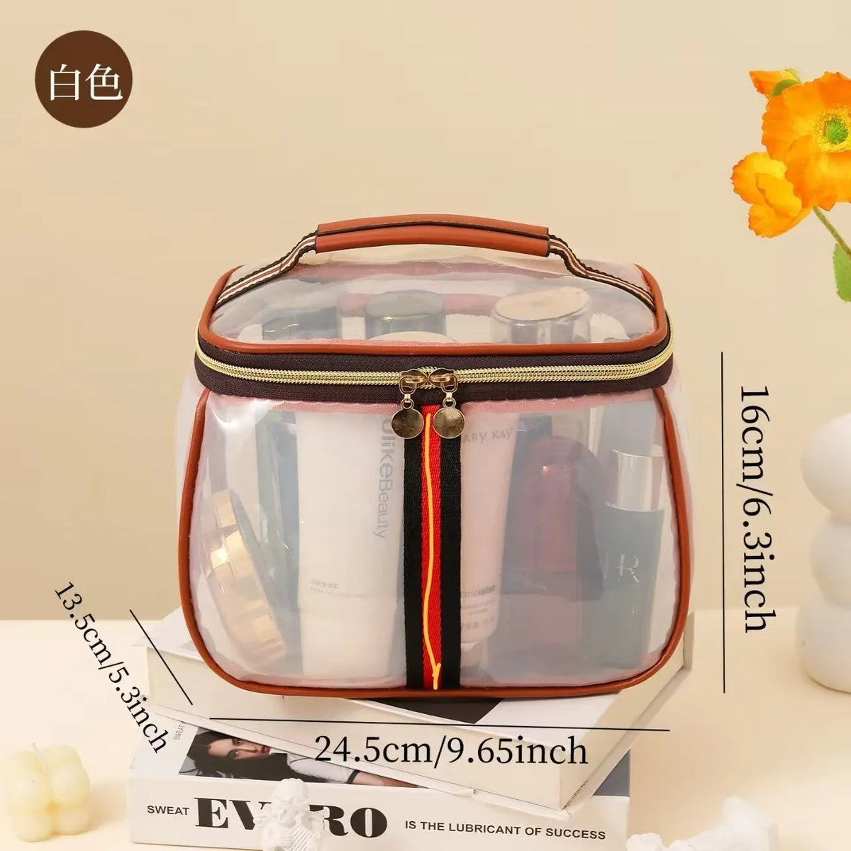 A clear waterproof travel toiletry bag with a brown and black trim resting on a stack of books.