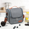 A gray insulated reusable lunch bag with an orange strap is shown on a white surface.