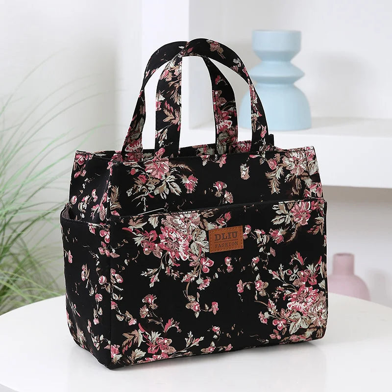 A black cloth tote bag with a pink floral pattern is displayed on a white surface.