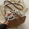 A close-up of a tan floral drawstring bucket bag with brown leather accents resting on a light fabric.