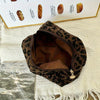 A brown leopard print makeup organizer bag lying on a white textured surface next to baked goods.