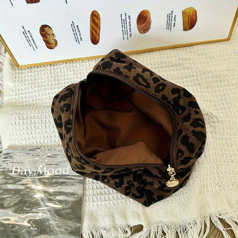 A brown leopard print makeup organizer bag lying on a white textured surface next to baked goods.