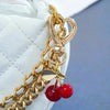 Gold chain charm featuring a heart and cherry blossom design attached to a white quilted bag.