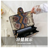 A close-up of an elegant retro crossbody bag with a patterned leather exterior and gold hardware, shown next to a hand.