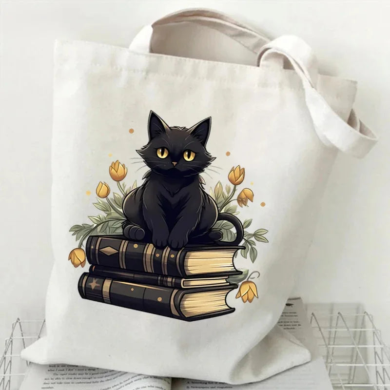 A white canvas tote bag featuring a black cat and golden butterfly print on the fabric.