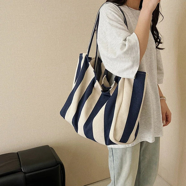 A woman holds a striped canvas tote bag with navy and cream stripes against a light background.