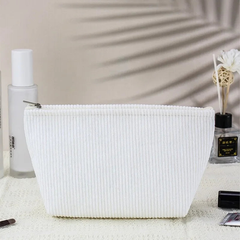 White corduroy makeup organizer bag with a vertical ribbed texture resting on a light surface.