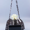 A handmade dumpling bag covered in silver and gold beads with a white ribbon, displayed next to a smartphone.