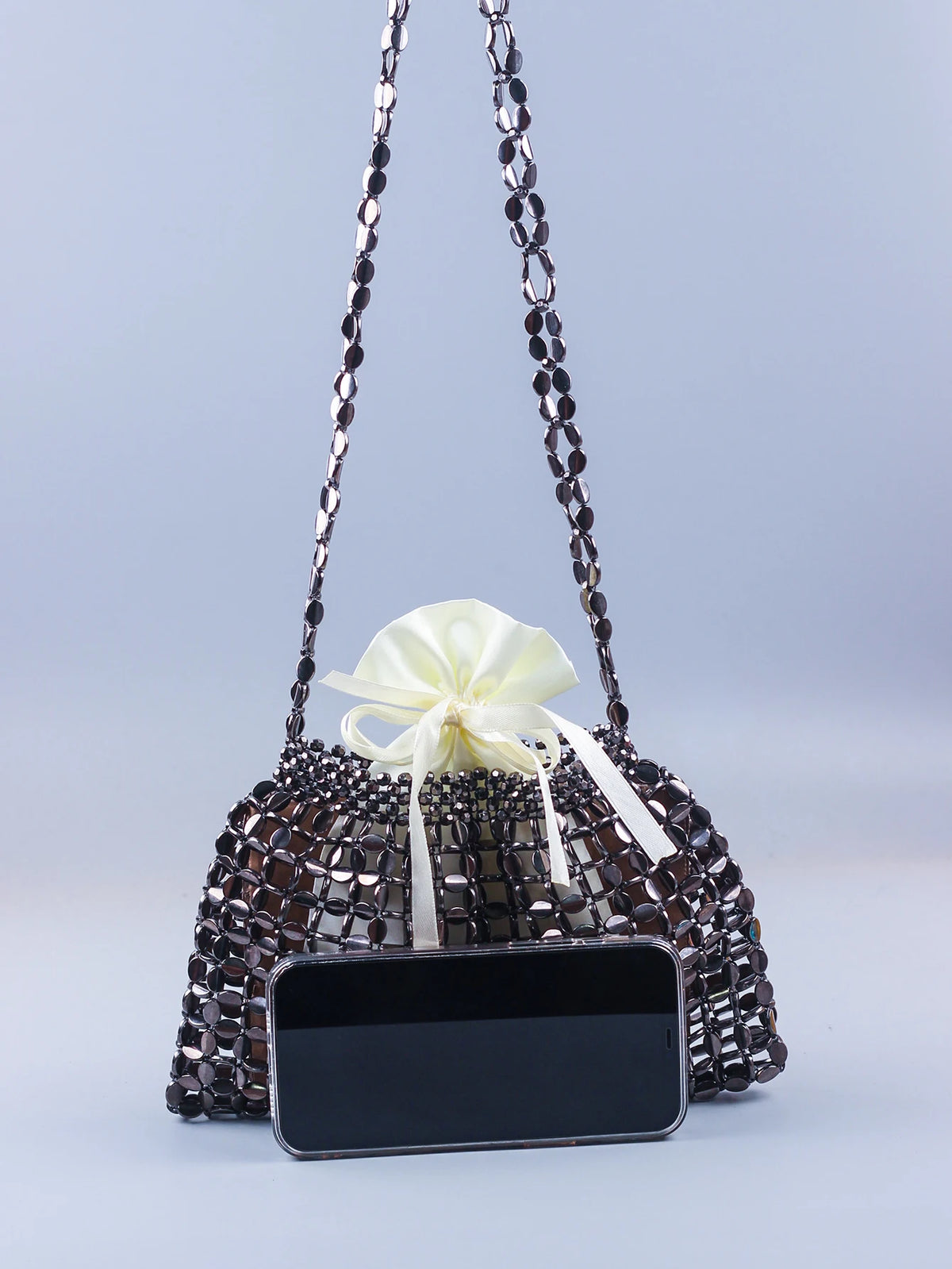 A handmade dumpling bag covered in silver and gold beads with a white ribbon, displayed next to a smartphone.