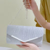 A hand holds a silver glitter pleated crossbody clutch bag with a detachable chain against a light background.