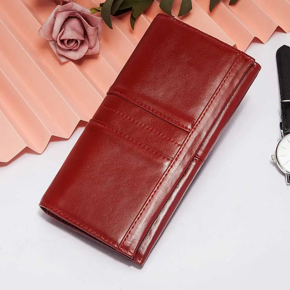A deep reddish-brown genuine leather clutch wallet is displayed on a white surface next to a pink rose and green leaves.