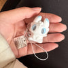 A white fluffy cat keychain pendant with blue eyes and a silver charm is held in a person's hand.