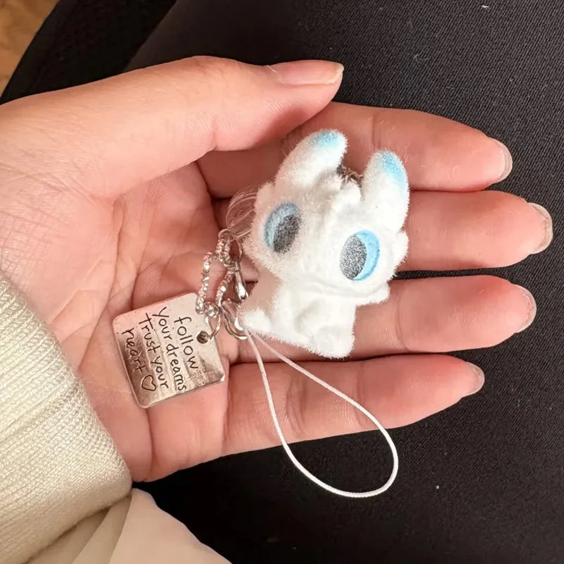 A white fluffy cat keychain pendant with blue eyes and a silver charm is held in a person's hand.