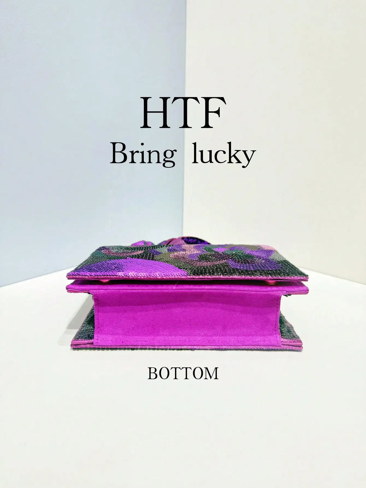A magenta clutch bag with purple sequin embroidery is displayed against a white background.