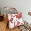 A pink faux fur designer shoulder tote bag with a white leopard print pattern resting on a wooden surface.