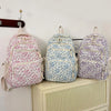 Three floral quilted backpacks in pink, blue, and purple are displayed on a shelf.