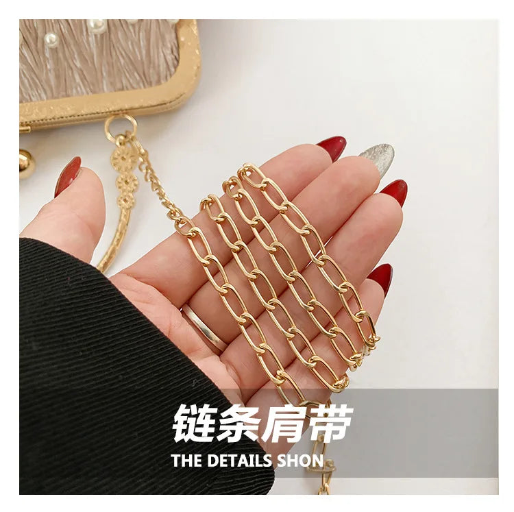 A hand holds a gold chain necklace with small beads and a gold pendant against a black fabric background.