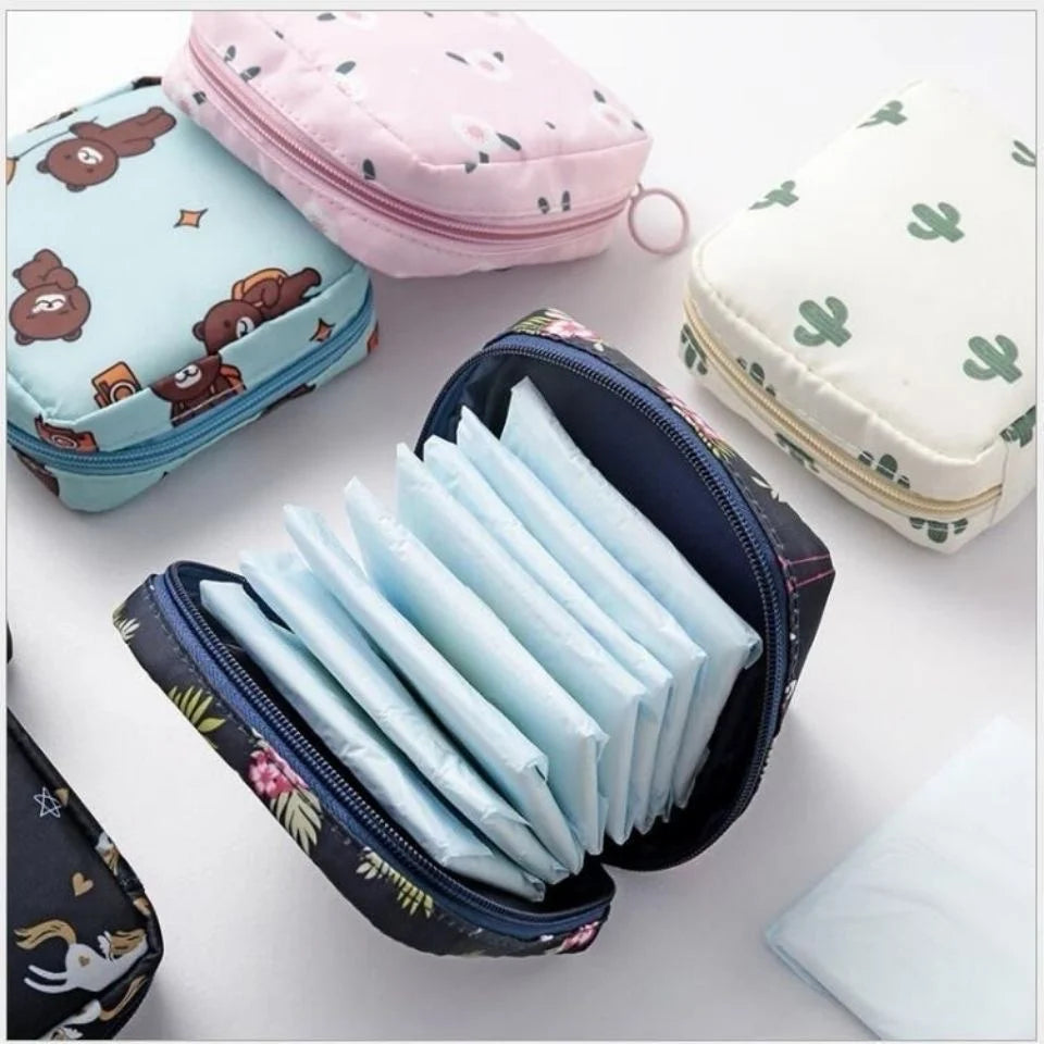 A collection of various colored and patterned compact sanitary pad storage pouches and a black zippered pouch filled with whi