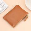 A brown genuine leather mini zipper coin and card purse lying on a light background next to a white computer keyboard.