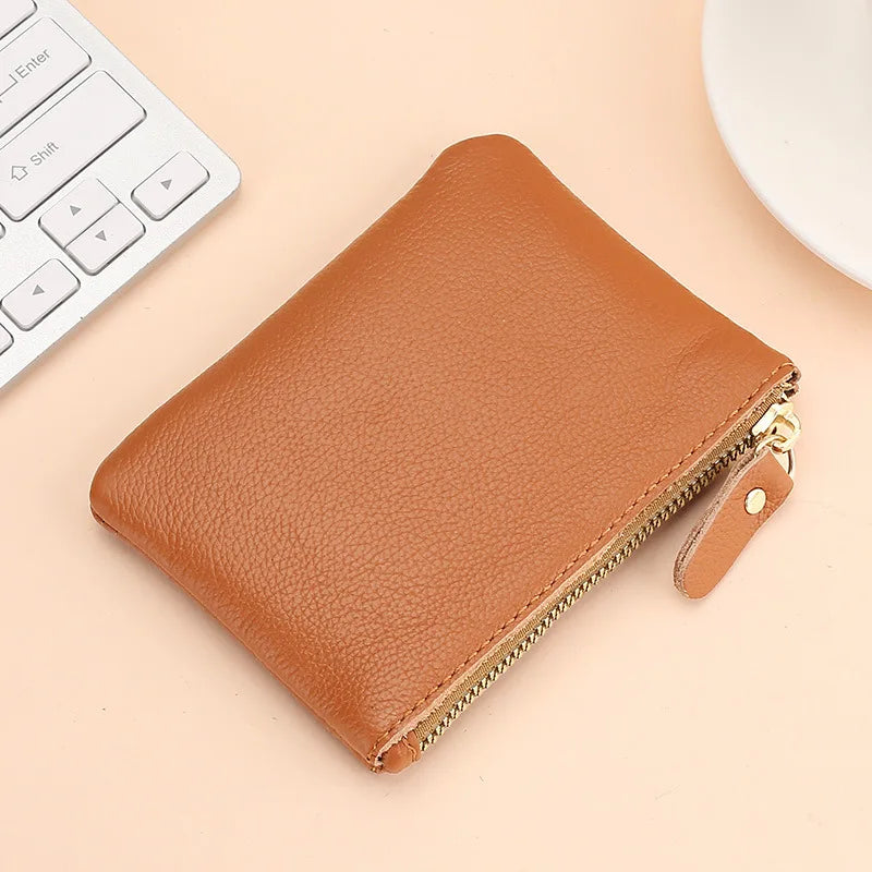 A brown genuine leather mini zipper coin and card purse lying on a light background next to a white computer keyboard.