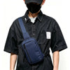 A person wearing a black shirt is carrying a navy blue chest bag across their body.