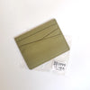 Porte-cartes en cuir vert avec gravure diagonale dans un emballage plastique transparent.