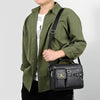 Un homme portant une chemise vert olive tient un sac bandoulière en similicuir noir.