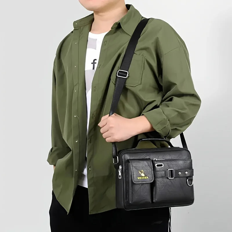 Un homme portant une chemise vert olive tient un sac bandoulière en similicuir noir.