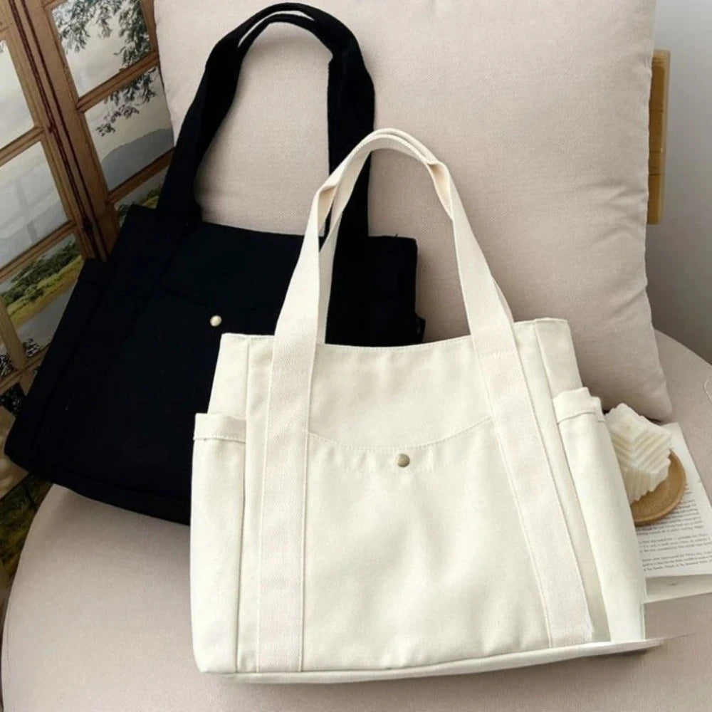 Una bolsa de tela blanca se muestra sobre una superficie clara junto a una bolsa de tela negra.