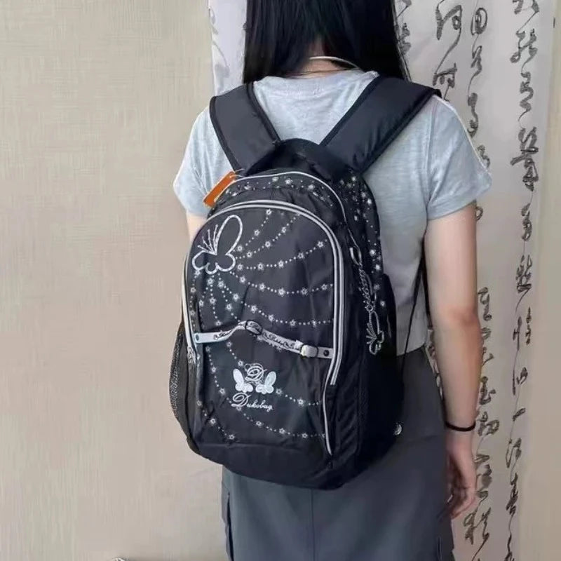 A person is wearing a black backpack with a butterfly print on the front against a light background.