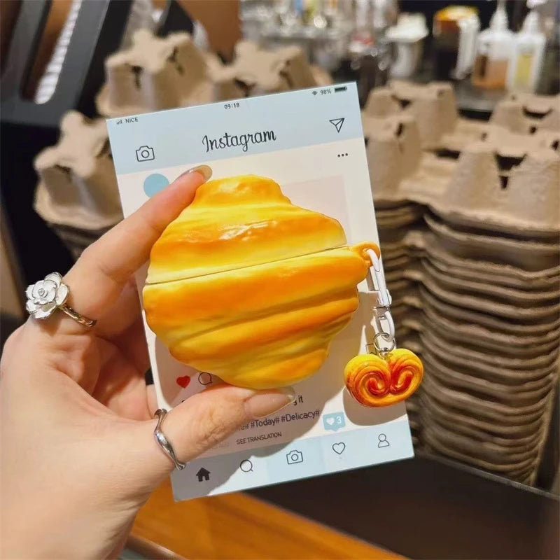 A hand holds a yellow silicone protective case for wireless earbuds against a blurred background of brown silicone products.