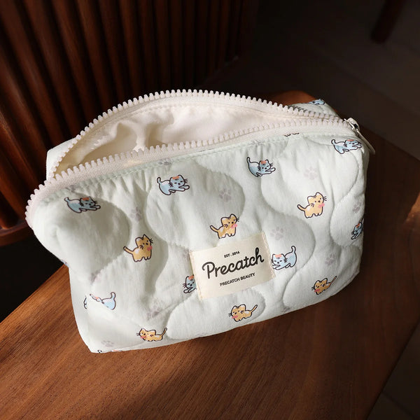 A white quilted cosmetic storage pouch featuring small printed cats on the exterior.