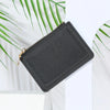 A black PU leather mini card holder wallet with a zipper closure is shown against a white background with green leaves.