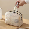 A hand is placing a glass bottle into a square, sheer lace mesh organizer bag.