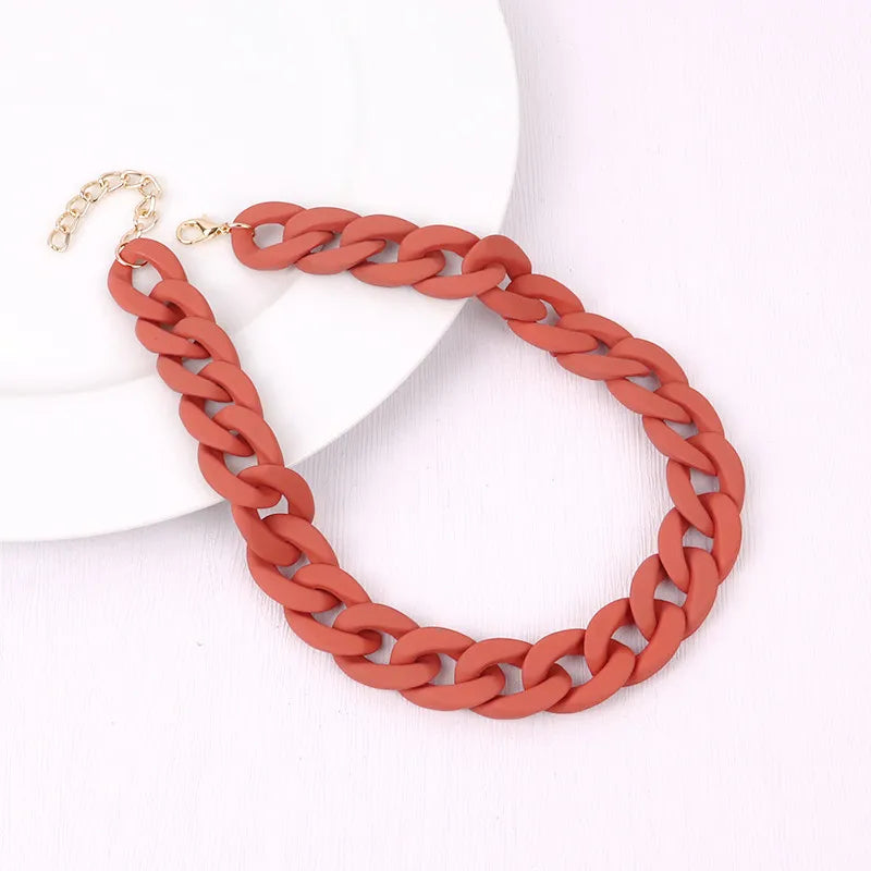 A close-up of a trendy orange acrylic statement choker necklace with a gold-colored clasp.
