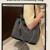 Eine Frau hält eine schwarze Diamant-Crossbody-Tasche mit silberner Kette vor einem hellgelben Hemd.