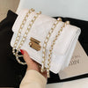 A white quilted crossbody bag with gold chain straps is held by a hand against a black background.
