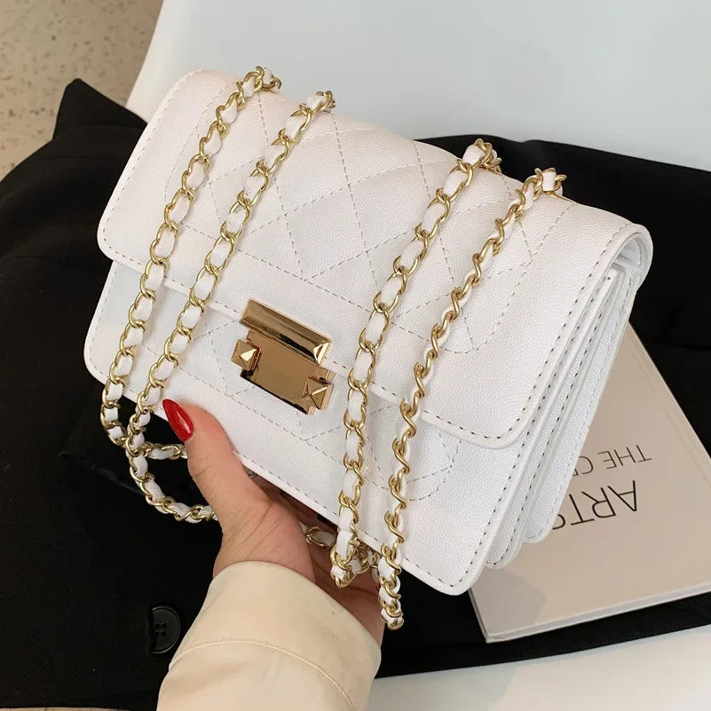 A white quilted crossbody bag with gold chain straps is held by a hand against a black background.