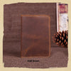 A dark brown genuine leather passport wallet with card holders resting on a textured brown surface.