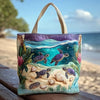 A purple and green quilted canvas tote bag featuring various sea turtle and seashell designs, resting on a wooden surface by 