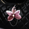 A realistic pink and purple phalaenopsis orchid flower keychain attached to a black quilted leather bag.